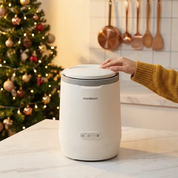 User hand touching the lid of a Moreborn kitchen waste processor next to a glowing Christmas tree.